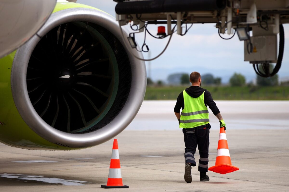 Airport worker moves cones near an airplane on a runway Airport worker moves cones near an airplane on a runway