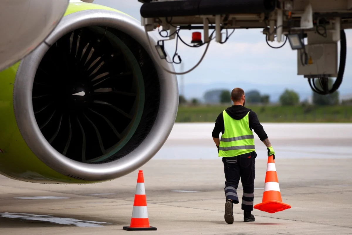 Airport worker moves cones near an airplane on a runway