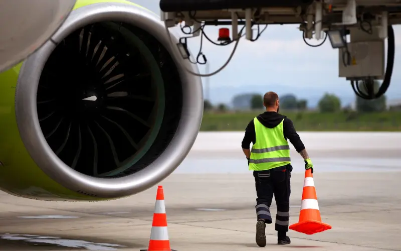 Airport worker moves cones near an airplane on a runway