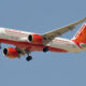 Air India passenger jet in white and orange livery taking off against a clear blue sky landing gear down and visible sunburst tail logo on the tail fin