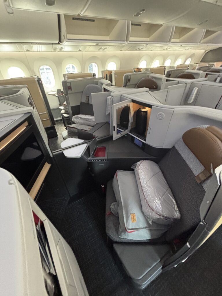 Business class airplane cabin with individual enclosed seating pods in gray and tan windows along the fuselage