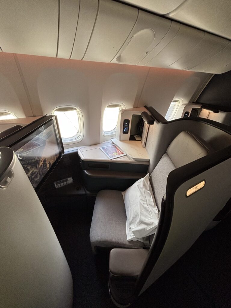 Business class airplane seat with a personal screen tray table and a white mask resting on the seat