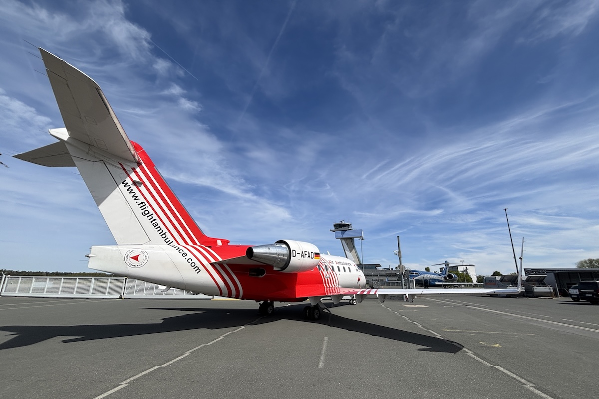 Red and white twin engine jet on a paved airport apron with a control tower in the background under a blue sky