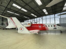 White and red ambulance aircraft parked inside a spacious hangar logo on the tail and fuselage visible