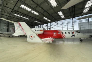 White and red ambulance aircraft parked inside a spacious hangar logo on the tail and fuselage visible