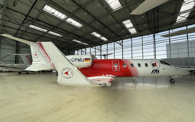 White and red ambulance aircraft parked inside a spacious hangar logo on the tail and fuselage visible