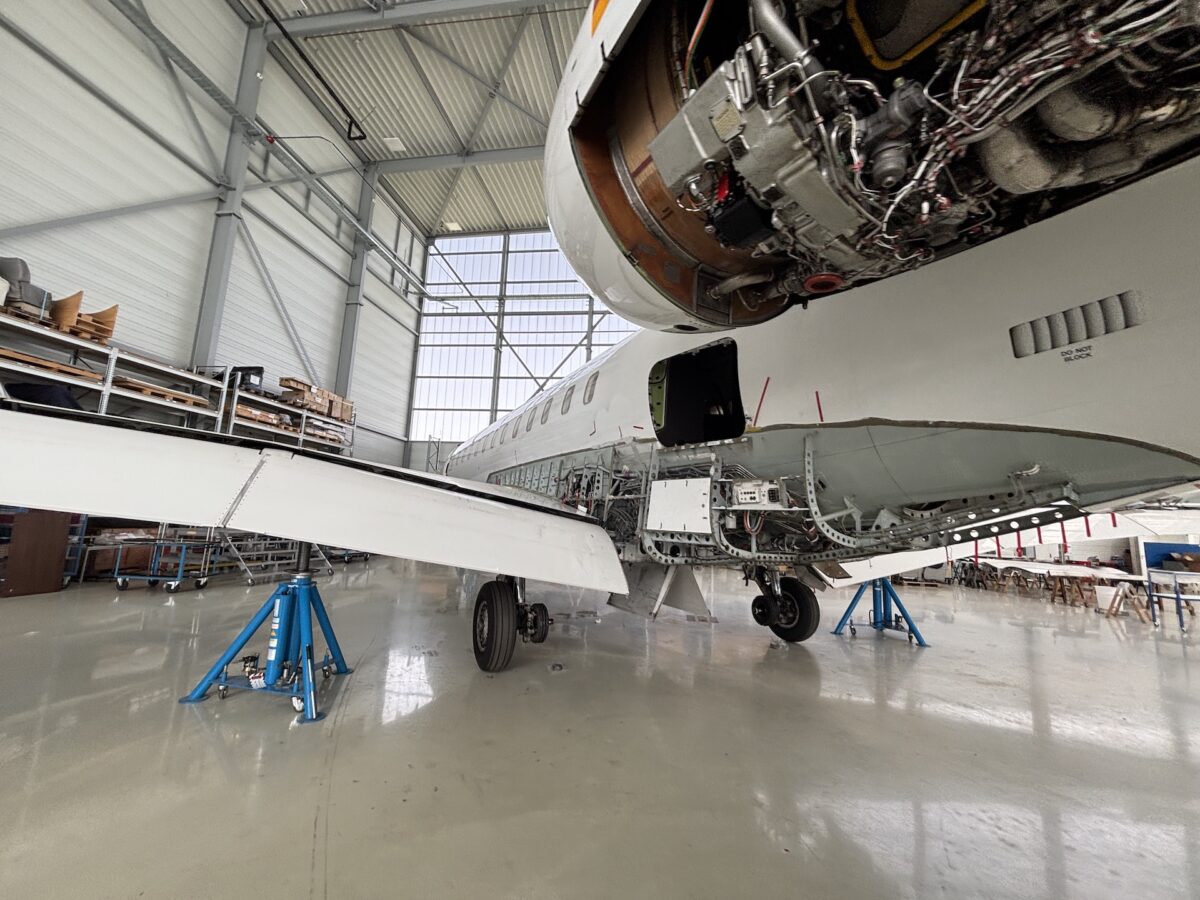 Maintenance hangar with a wide wing aircraft on jacks engine cowl removed exposing wiring and components workshop in background