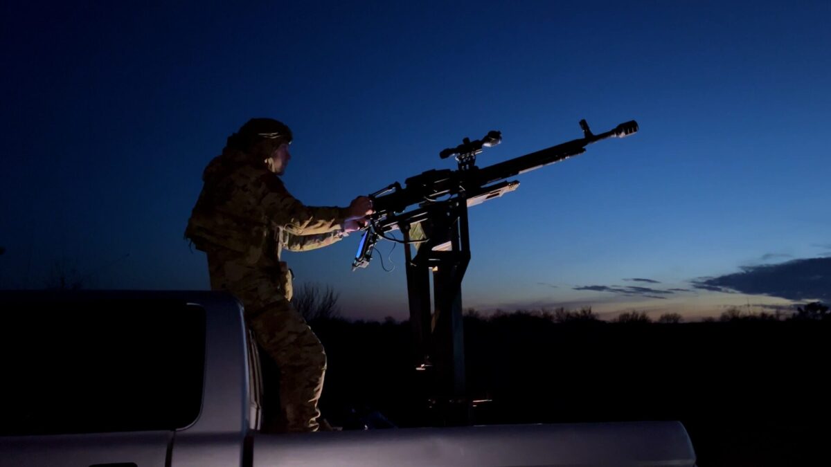 KharkivUkraine February272024ASoldierStandsIn Soldier in camouflage stands in the back of a pickup truck manning a large mounted weapon against a dark blue dusk sky