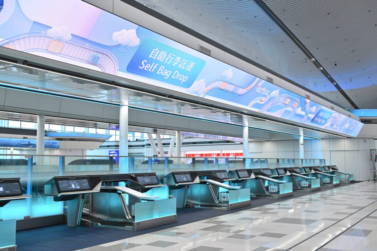 Self bag drop counters Row of self check in kiosks in a bright airport terminal with turquoise accents and a large blue sign reading Self Bag Drop