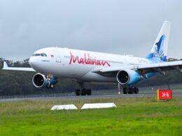 Maldives A330 aircraft on a runway with landing gear down and a blue tinted tail design visible behind trees