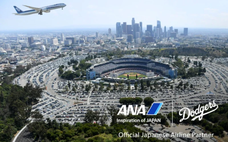 Aerial view of downtown Los Angeles with Dodger Stadium in the foreground and an ANA airplane taking off in the blue sky above