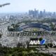 Aerial view of downtown Los Angeles with Dodger Stadium in the foreground and an ANA airplane taking off in the blue sky above
