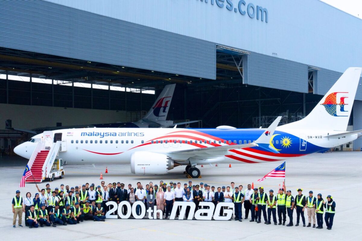 Group of Malaysia Airlines staff and engineers posing with a colorful jet inside a hangar in front of a large 200th MAG banner