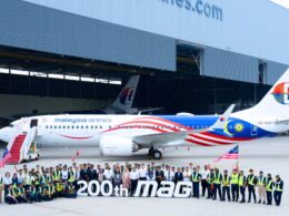 Group of Malaysia Airlines staff and engineers posing with a colorful jet inside a hangar in front of a large 200th MAG banner