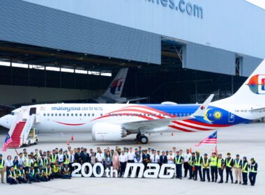 Group of Malaysia Airlines staff and engineers posing with a colorful jet inside a hangar, in front of a large '200th MAG' banner.