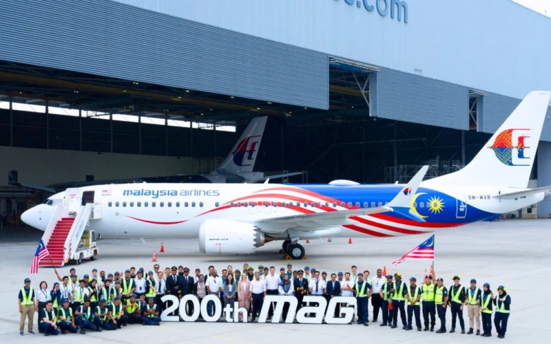 Group of Malaysia Airlines staff and engineers posing with a colorful jet inside a hangar in front of a large 200th MAG banner