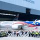 Group of Malaysia Airlines staff and engineers posing with a colorful jet inside a hangar in front of a large 200th MAG banner
