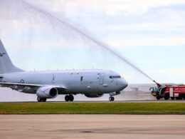 White military jet on a tarmac with a fire truck spraying a water arc over its fuselage in a takeoffarrival scene