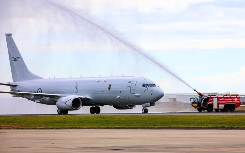 14th Royal Australian Air Force P 8A Poseidon White military jet on a tarmac with a fire truck spraying a water arc over its fuselage in a takeoffarrival scene