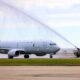 White military jet on a tarmac with a fire truck spraying a water arc over its fuselage in a takeoffarrival scene