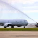 White military jet on a tarmac with a fire truck spraying a water arc over its fuselage in a takeoffarrival scene
