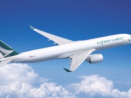 Cathay Cargo airplane in flight with a teal logo on the tail soaring above white clouds in a bright blue sky