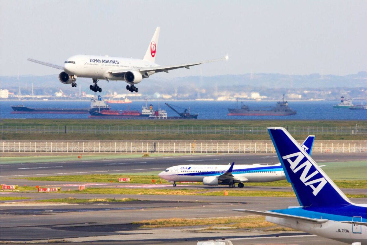 ANA and JAL Japan Airlines jet landing over a harbor with ships on the water and an ANA tail in the foreground