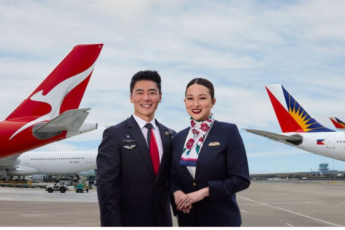 Two airline crew members a man and a woman in dark uniforms stand smiling on a runway with red and white aircraft tails in the background