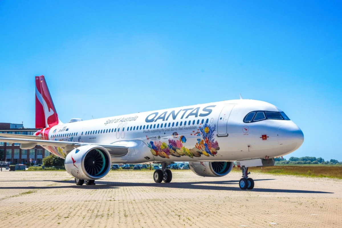 Qantas A321XLR Great Barrier Reef livery Qantas airplane parked on a tarmac with vibrant coral reef artwork along its fuselage and a bright blue sky above