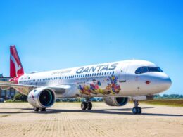 Qantas airplane parked on a tarmac with vibrant coral reef artwork along its fuselage and a bright blue sky above