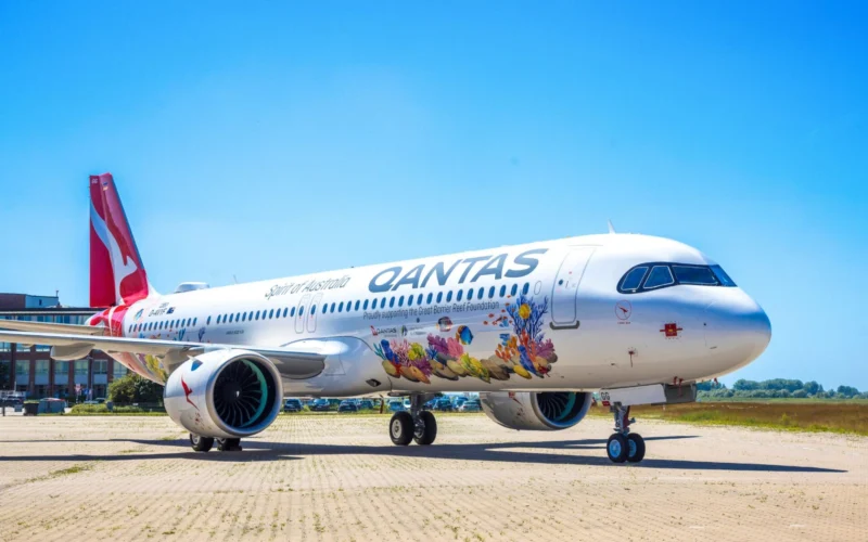 Qantas airplane parked on a tarmac with vibrant coral reef artwork along its fuselage and a bright blue sky above