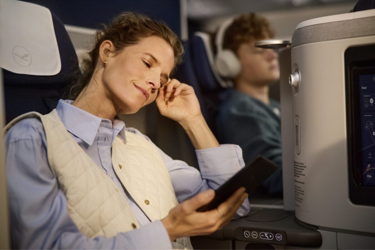 Lufthansa expands Allegris to more destinations Woman asleep with hand to temple holding a tablet wearing a light quilted vest over a blue shirt on an airplane seat