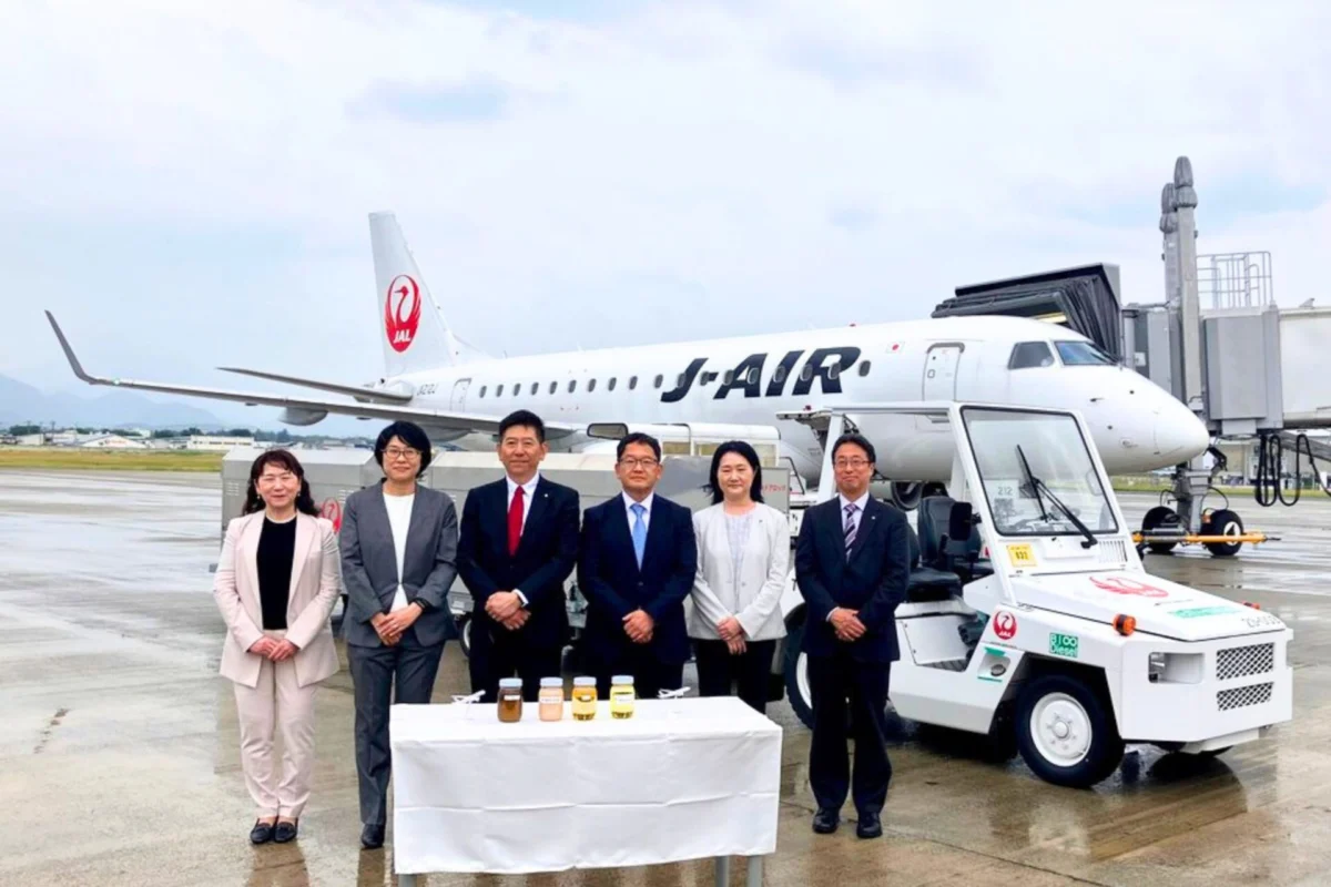JAL tests 1st biodiesel from rice bran oil Seven professionals in business attire stand in a line in front of a Japan Airlines jet at the gate with a table of bottled drinks in front