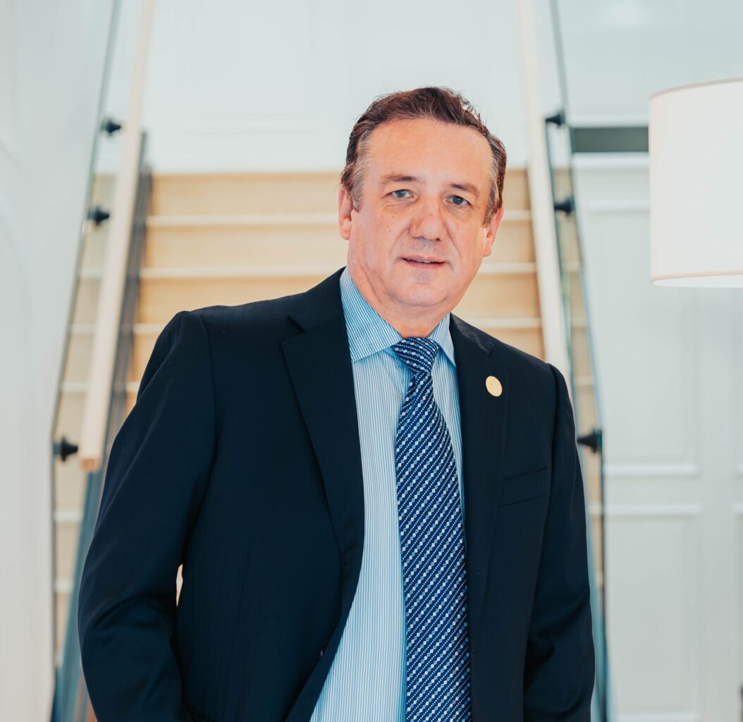 Portrait of a middle aged man in a dark suit and blue striped tie standing on a bright indoor staircase looking at the camera