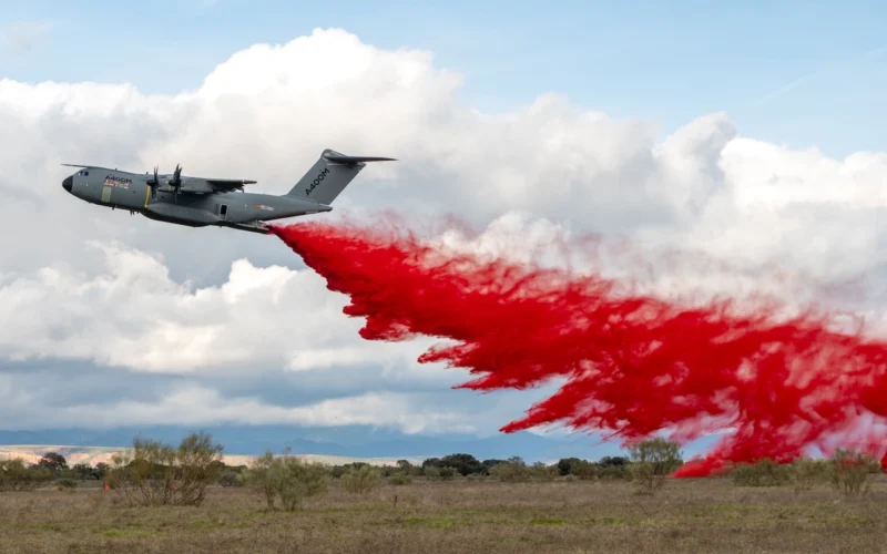 Military transport airplane releasing bright red smoke trail over an open field