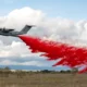 Military transport airplane releasing bright red smoke trail over an open field