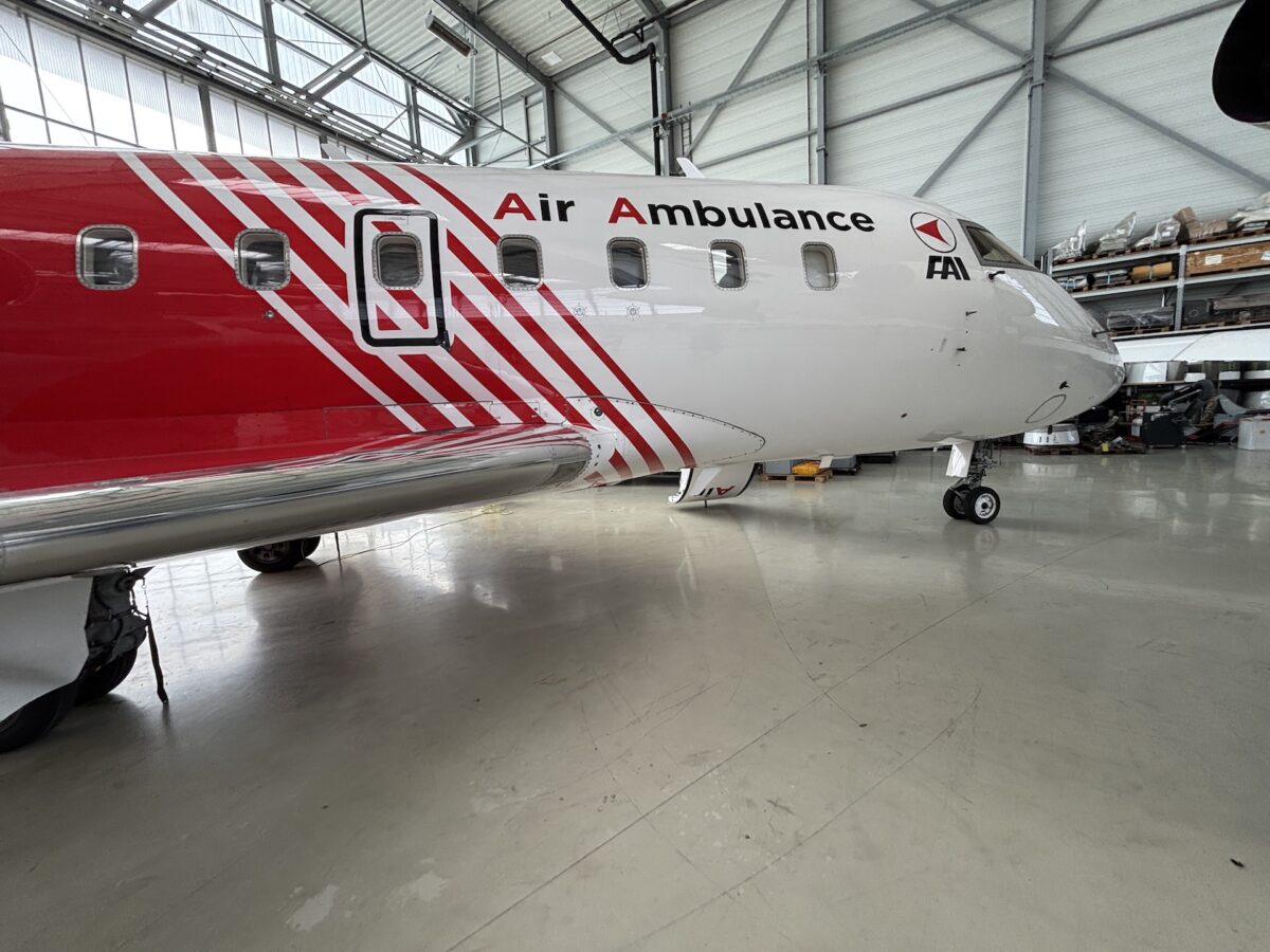 Side view of an air ambulance aircraft inside a hangar red and white livery with diagonal stripes and Air Ambulance lettering on the fuselage