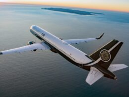 White private jet with Magnifica Air branding banks over the calm ocean at sunset with distant islands on the horizon