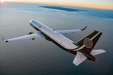 White private jet with Magnifica Air branding banks over the calm ocean at sunset with distant islands on the horizon