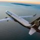 White private jet with Magnifica Air branding banks over the calm ocean at sunset with distant islands on the horizon