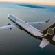 White private jet with Magnifica Air branding banks over the calm ocean at sunset with distant islands on the horizon