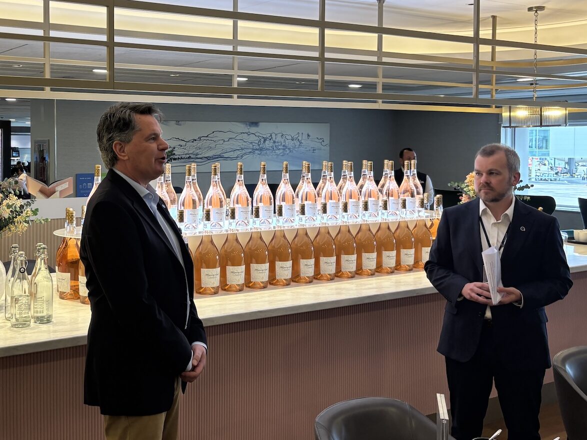 oneworld lounge event lhr Two men in suits stand by a bar displaying dozens of rosé bottles in a modern event space