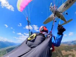 Paraglider in midflight with a small plane flying overhead against a blue sky