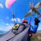 Paraglider in midflight with a small plane flying overhead against a blue sky