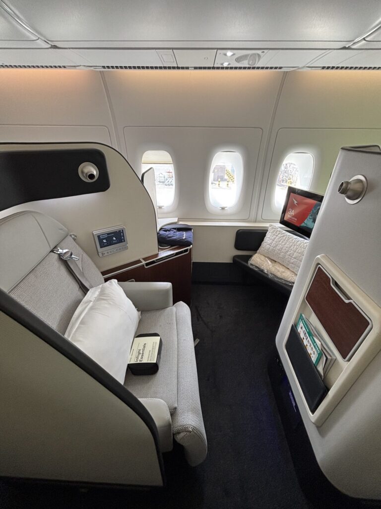 Private business class seating area with a curved beige partition a cushioned seat and reading light a windowed wall with multiple oval windows ahead