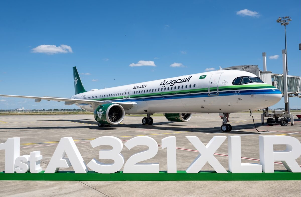 saudia a321xlr Saudia Airbus A321XLR parked at the gate with a green and blue stripe livery under a blue skyFront right view of a Saudia A321XLR at the jet bridge white fuselage with green tail and logoLarge 1st A321XLR signage on the ground in front of the parked airliner on the tarmac