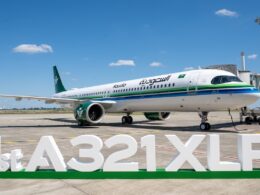 Saudia Airbus A321XLR parked at the gate with a green and blue stripe livery under a blue skyFront right view of a Saudia A321XLR at the jet bridge white fuselage with green tail and logoLarge 1st A321XLR signage on the ground in front of the parked airliner on the tarmac