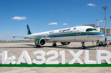 Saudia Airbus A321XLR parked at the gate with a green and blue stripe livery under a blue skyFront right view of a Saudia A321XLR at the jet bridge white fuselage with green tail and logoLarge 1st A321XLR signage on the ground in front of the parked airliner on the tarmac