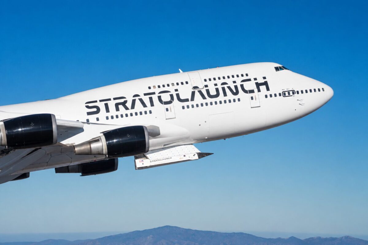 strat32 White Stratolaunch aircraft in flight against a clear blue sky with distant mountains on the horizon and its branding visible on the fuselage