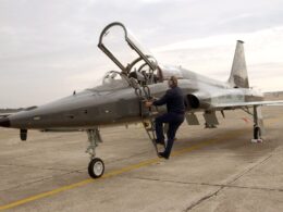 US Air Force fighter jet on a tarmac with the cockpit canopy open and a ground crew member climbing a ladder toward the cockpit